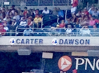 Stadium seating filled with spectators during what appears to be a sporting event, with visible advertising signage including "CARTER," "DAWSON," and "PNC" logos along the venue wall.